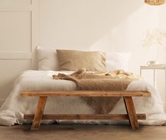 a bed with pillows and blankets on top of it next to a wooden bench in front of a white wall