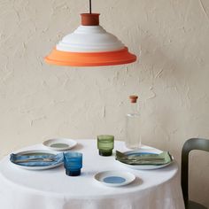 a white table topped with plates and bowls next to a light hanging from the ceiling