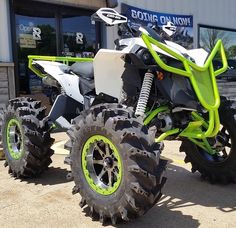 a white and green four wheeler parked in front of a building with two large tires