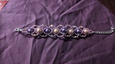 a purple bracelet with pearls and chains on top of a purple cloth covered tablecloth