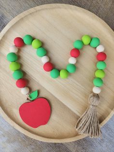 a wooden tray with an apple and tasseled beads on it, next to a string of fruit