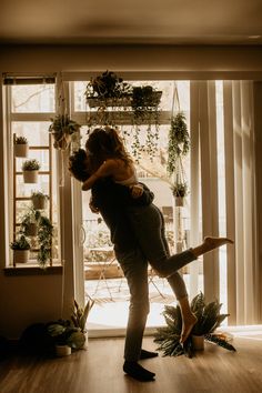 a man and woman kissing in front of a window with plants on the windowsill