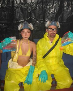 a man and woman dressed in yellow sitting on a blue couch with plastic bags over their heads