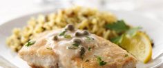 a white plate topped with meat covered in gravy next to pasta and lemon wedges