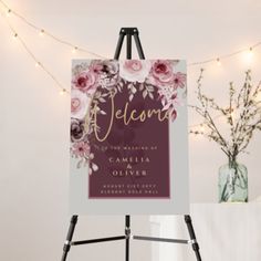 an easel with a welcome sign on it and flowers in front of a string of lights