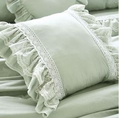 a bed with two pillows and some lace on the pillowcase, one is light green