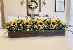 sunflowers and greenery are arranged in a wooden planter on the table