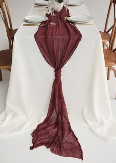 the table is set with white plates and wine glasses, napkins, and a red scarf