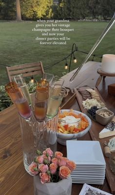 there is a table with food and drinks on it that includes wine glasses, cheeses, crackers, and flowers