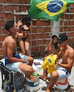 some people are sitting on the side of a brick building and one person is holding a yellow shirt