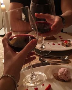 two people are toasting with red wine in front of each other at a dinner table