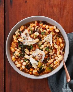 a white bowl filled with beans and greens on top of a wooden table next to a spoon