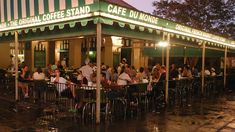 a group of people sitting at tables in front of a cafe on a rainy night