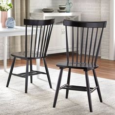 two black chairs sitting on top of a white rug in front of a kitchen table