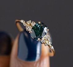 a woman's hand holding a ring with a green stone and white diamonds on it