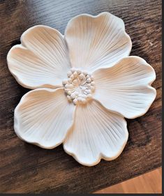 a white flower shaped dish sitting on top of a wooden table