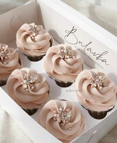 six cupcakes with pink frosting and pearls in a white box on a table