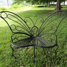 a metal bench in the grass with a butterfly design on it's back end