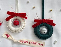 three christmas ornaments are hanging on a white table cloth with red ribbon and bells attached to them