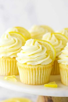 several cupcakes with white frosting and lemon wedges on a cake plate