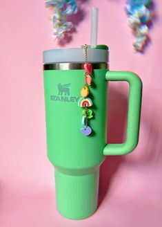 a green coffee cup with a straw in it and beads hanging from the handle, on a pink background