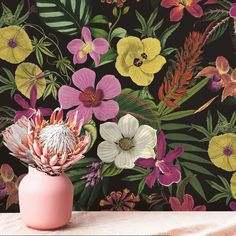 a pink vase filled with flowers on top of a table next to a floral wallpaper