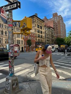 a woman walking across a street next to a traffic light and cross walk sign with buildings in the background