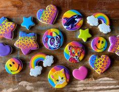 decorated cookies with different designs and colors on a wooden surface, including hearts, stars, rainbows, cats, fish, and more