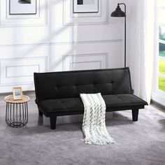 a black futon sofa sitting in a living room next to a table and lamp