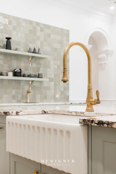 a kitchen sink with gold faucet and marble counter tops in front of shelves