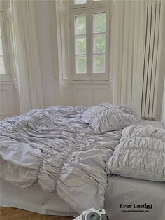 an unmade bed with white sheets and pillows in a bedroom next to a window