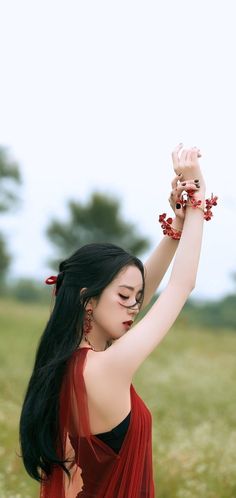 a woman with long black hair wearing a red dress and holding her arm up in the air