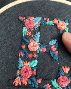 someone is stitching the letters on a piece of fabric with flowers and leaves in it