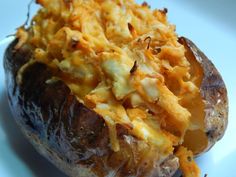 a baked potato with cheese on it sitting on a white plate next to a fork