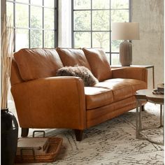 a brown leather couch sitting on top of a rug in a living room next to a window