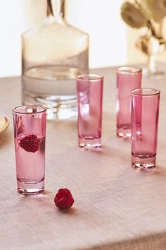 four glasses with raspberries in them sitting on a table next to a vase