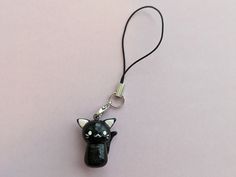 a black cat keychain hanging from a cord on a pink surface with a white background