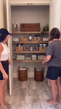 two women standing in the doorway of a bathroom looking at towels and other items on shelves