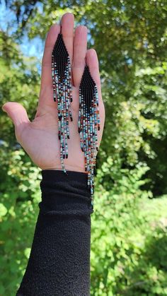 a woman's hand holding two pairs of beaded earrings in front of trees