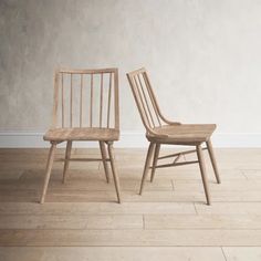 two wooden chairs sitting next to each other on top of a hard wood floor in front of a white wall