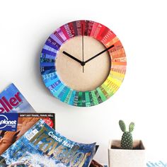 a colorful clock on the wall next to some magazines and a cacti in a pot