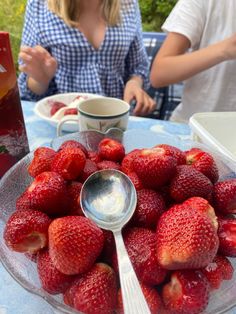 a bowl of strawberries on a table with two people in the background