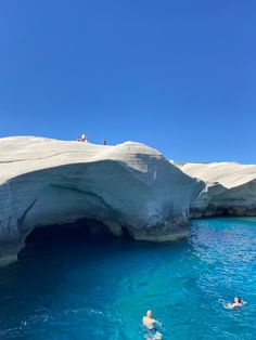 two people swimming in the ocean near an ice cave