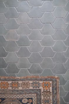 a rug sitting on top of a wooden floor in front of a wall with hexagonal tiles