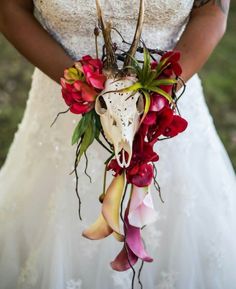 a woman in a wedding dress holding a bouquet with flowers and a deer skull on it