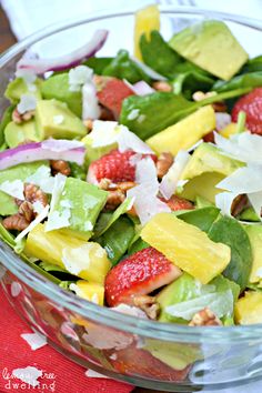 a salad with strawberries, pineapples and nuts in a glass bowl on a red napkin