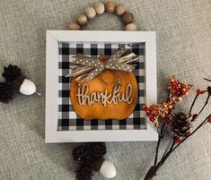 an orange pumpkin with a bow on it sitting in a frame next to some pine cones