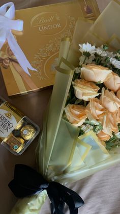 a bouquet of flowers and chocolates on a bed next to an unopened box