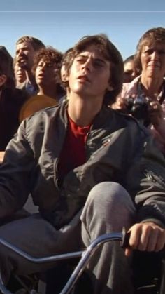 a group of people sitting next to each other in front of a man on a motorcycle