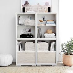 a white bookcase with books and magazines on it next to a potted plant